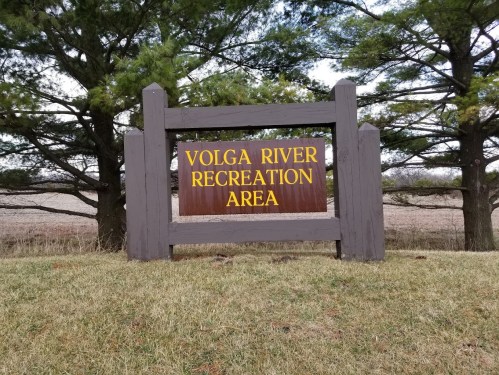 Sign for Volga River Recreation Area, framed by trees and grassy field in the background.