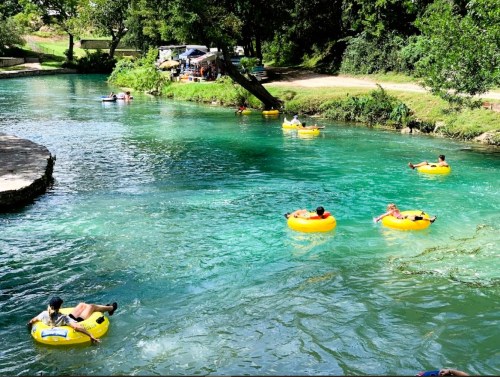 People floating on yellow inner tubes in a clear, turquoise river surrounded by lush greenery.