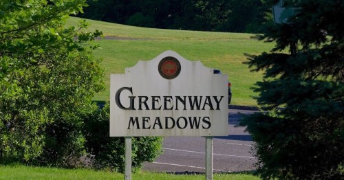 Sign for Greenway Meadows, surrounded by greenery and a grassy area in the background.