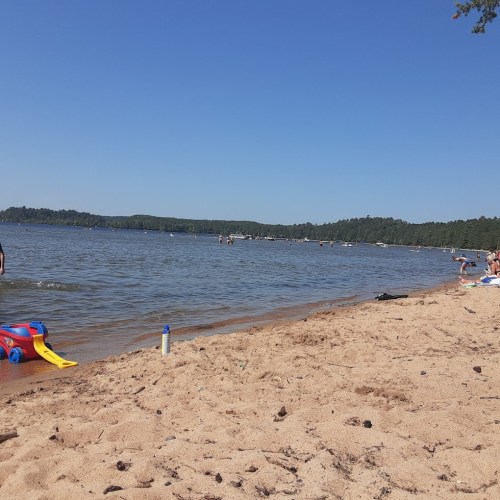 A sandy beach with people enjoying the water, boats in the distance, and clear blue skies.
