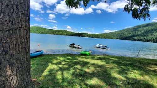 A serene lake scene with boats on the water, surrounded by green hills and a clear blue sky with fluffy clouds.