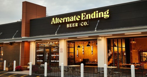 Exterior of Alternate Ending Beer Co. with a modern design and illuminated sign, featuring large windows and outdoor seating.