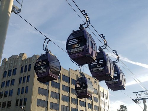 A row of purple gondolas suspended on cables against a clear sky, with a building in the background.