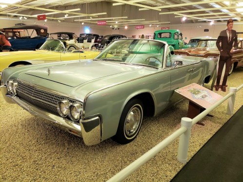 A vintage light blue convertible car displayed in a museum, surrounded by other classic vehicles.