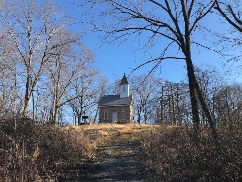A small church on a hill surrounded by bare trees under a clear blue sky.