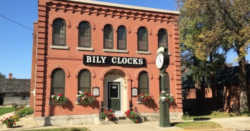 Historic brick building with arched windows, a clock tower, and flower boxes, labeled "Bily Clocks."