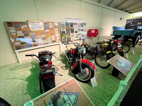 A display of vintage motorcycles and license plates in a museum setting, showcasing Arkansas license plates and historical vehicles.