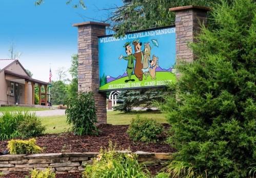 A colorful welcome sign for Jellystone Park, featuring cartoon characters and surrounded by greenery and landscaping.