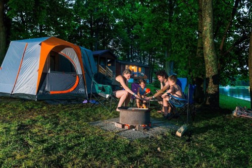 A family gathers around a campfire at night, enjoying time together near their tent and a serene lake.