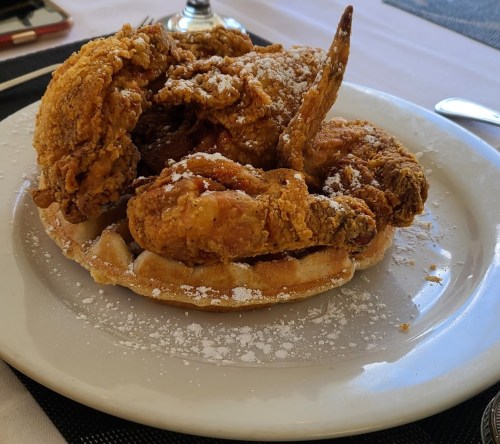 A plate of crispy fried chicken served on a waffle, dusted with powdered sugar.