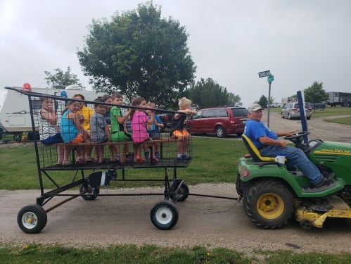 A man drives a tractor pulling a cart filled with children, enjoying a fun ride on a cloudy day.