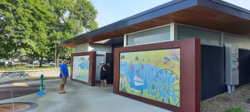A modern building with colorful murals depicting Iowa scenes, surrounded by greenery and a playground area.