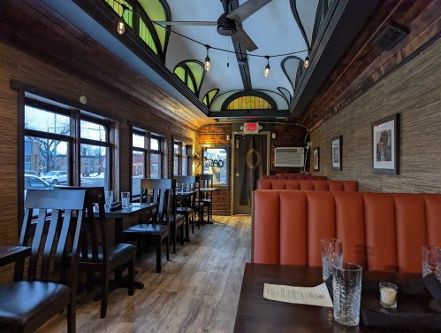 Cozy restaurant interior with wooden accents, orange booths, and large windows, featuring a unique ceiling design.