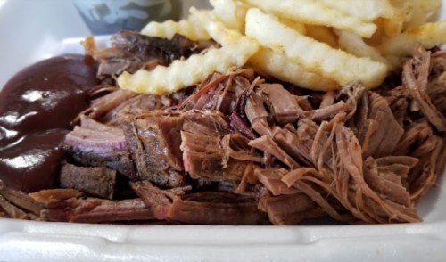Close-up of shredded beef with barbecue sauce and crinkle-cut fries in a takeout container.