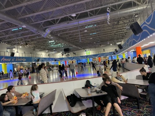 A busy roller skating rink with colorful walls, people skating, and others sitting at tables.