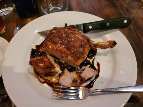 A plated dish featuring a roasted chicken breast with crispy skin, served with a side of dark sauce and garnished.