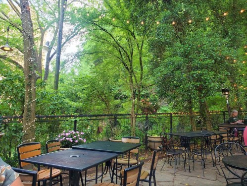 A serene outdoor dining area with tables, surrounded by lush greenery and string lights, creating a cozy atmosphere.