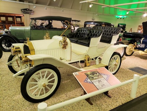 A vintage white car with gold accents and a black leather interior displayed in a museum setting.