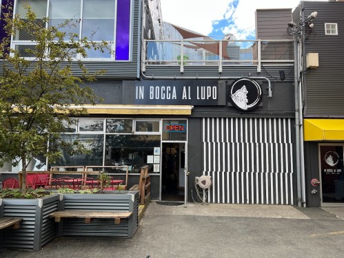 Exterior of a restaurant named "In Bocca Al Lupo," featuring a black facade, striped entrance, and an "Open" sign.