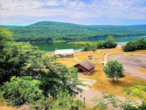 Scenic view of a lake surrounded by green hills, with a picnic area and parking lot in the foreground.