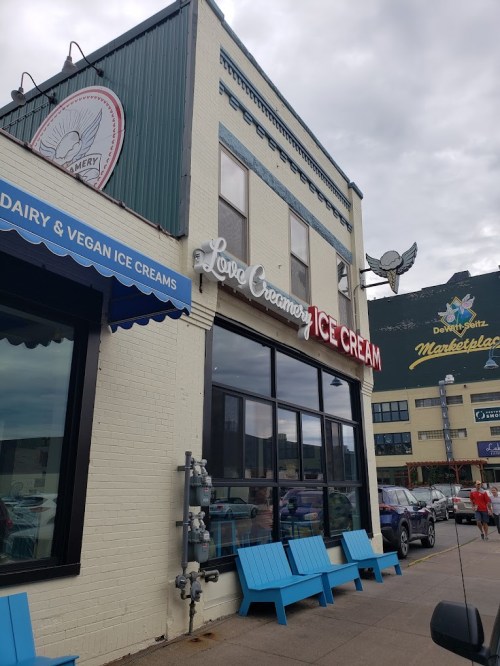 Exterior of Love Creamery ice cream shop, featuring blue seating and a cloudy sky in the background.