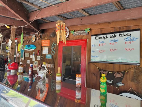 A rustic seafood counter displaying crab prices, with colorful decorations and condiments on the bar.