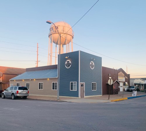A two-tone building with a water tower in the background, located in a small town. Clear sky above.