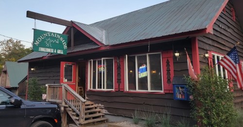 A rustic restaurant with a wooden exterior, red accents, and a sign reading "Mountain Side" in a scenic setting.