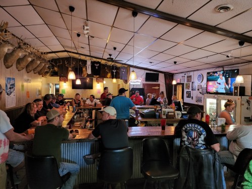 A lively bar scene with patrons seated at the counter, chatting and enjoying drinks in a rustic setting.