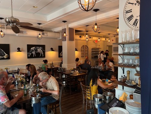 A bustling restaurant interior with diners at tables, warm lighting, and artwork on the walls.