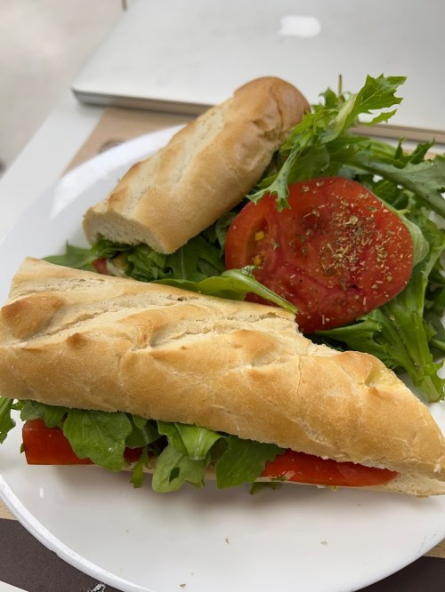 A plate with a sandwich made of crusty bread, filled with lettuce and tomato, alongside a fresh salad.