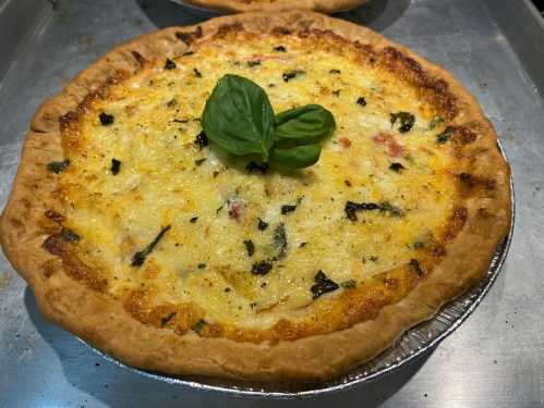 A freshly baked pizza with a golden crust, topped with cheese, herbs, and a basil leaf in the center.