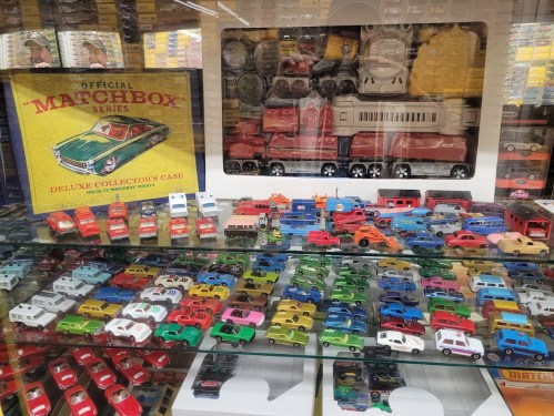 A display case filled with colorful Matchbox toy cars, featuring a variety of models and a collector's case in the background.