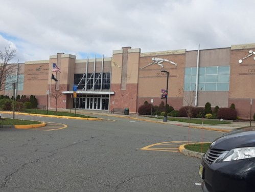 Exterior view of a large sports complex with flags, parking lot, and cloudy sky in the background.