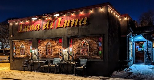 A cozy restaurant exterior at night, adorned with string lights and colorful window decorations.