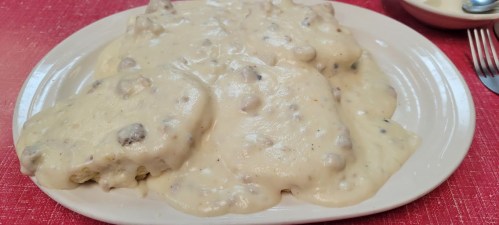 A plate of biscuits smothered in creamy sausage gravy, served on a red tablecloth.