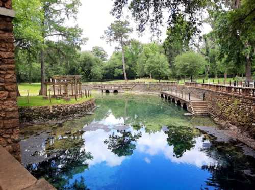 A serene landscape featuring a clear blue pond, wooden bridges, and lush green trees reflecting in the water.