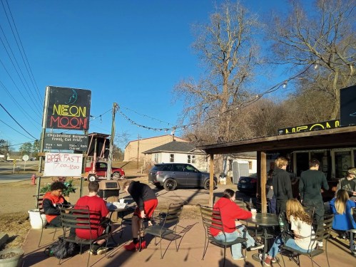 A busy outdoor dining area at Neon Moon, featuring people enjoying burgers under a clear blue sky.