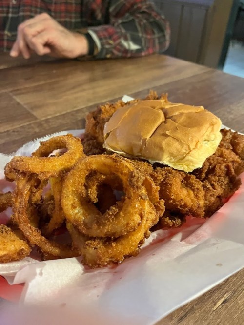 A plate of crispy fried chicken sandwich with onion rings on a red and white checkered paper.