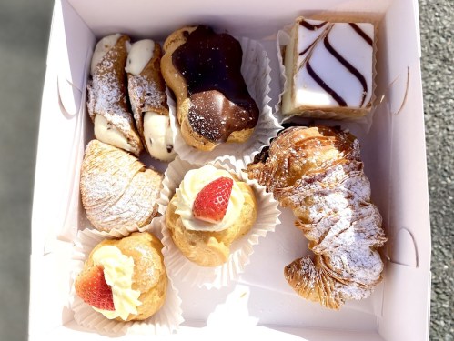 A box of assorted pastries, including cream-filled puffs, chocolate-covered treats, and croissants topped with strawberries.