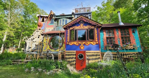 A colorful, whimsical house surrounded by greenery, featuring unique architectural details and vibrant decorations.