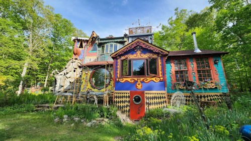 A colorful, whimsical house surrounded by greenery, featuring unique architectural designs and vibrant patterns.