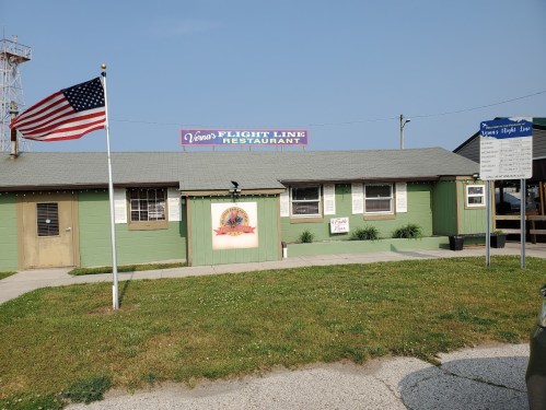 Exterior of Vena's Flight Line Restaurant with an American flag, green walls, and a sign above the entrance.