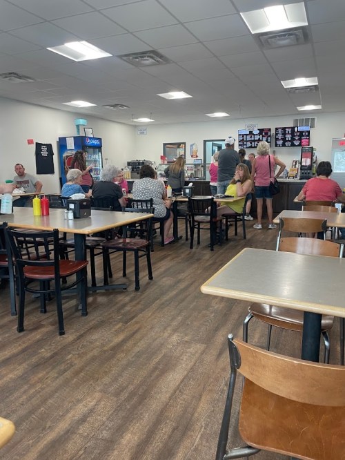 A busy diner interior with patrons seated at tables and a counter, featuring drinks and condiments on the tables.