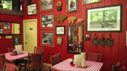 Cozy restaurant interior with red walls, vintage photos, and a checkered tablecloth on a small table.