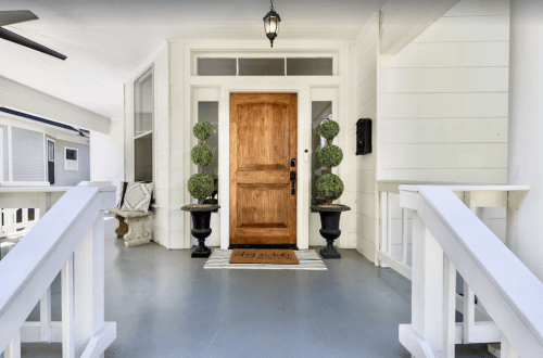 A welcoming front porch with a wooden door, potted topiaries, and a decorative mat.
