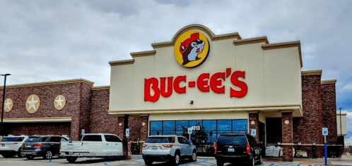 Exterior of a Buc-ee's convenience store with a large logo, featuring a beaver mascot and parked vehicles in front.