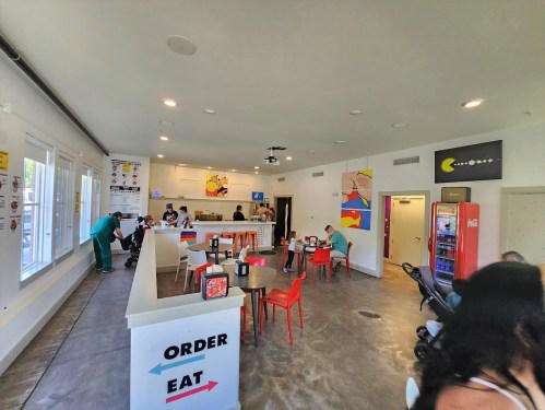 A bright, modern restaurant interior with colorful decor, seating areas, and customers ordering at the counter.