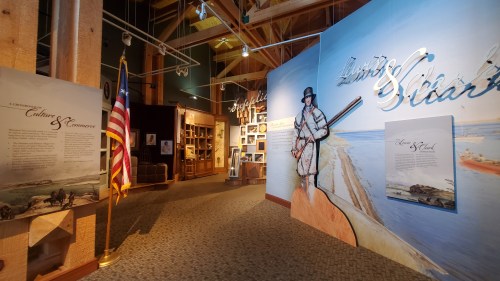 Interior of a museum exhibit featuring a large mural of a man with a fishing rod, alongside informational displays and an American flag.
