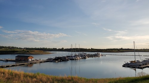A serene marina at sunset, featuring boats docked in calm waters and a clear sky with scattered clouds.